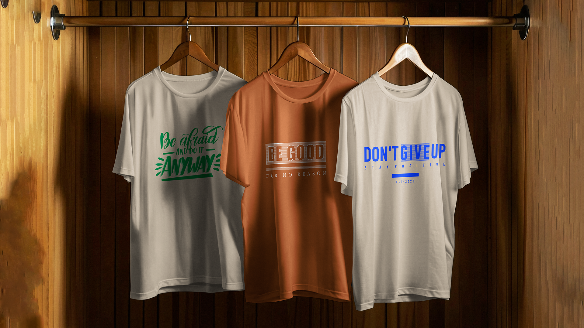 Three custom staple t-shirts with motivational phrases on hangers against a wooden wall